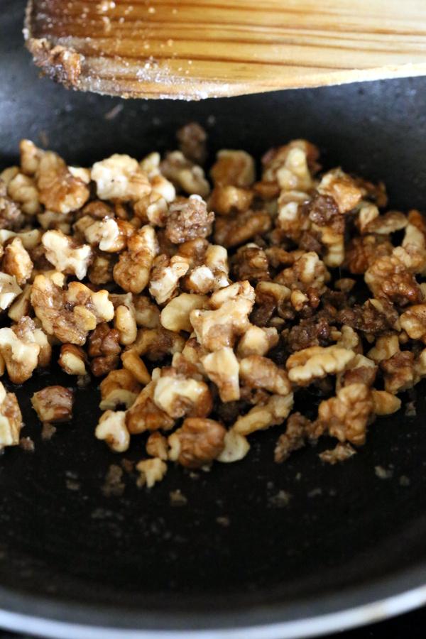 walnuts being candied in a frying pan with raw sugar