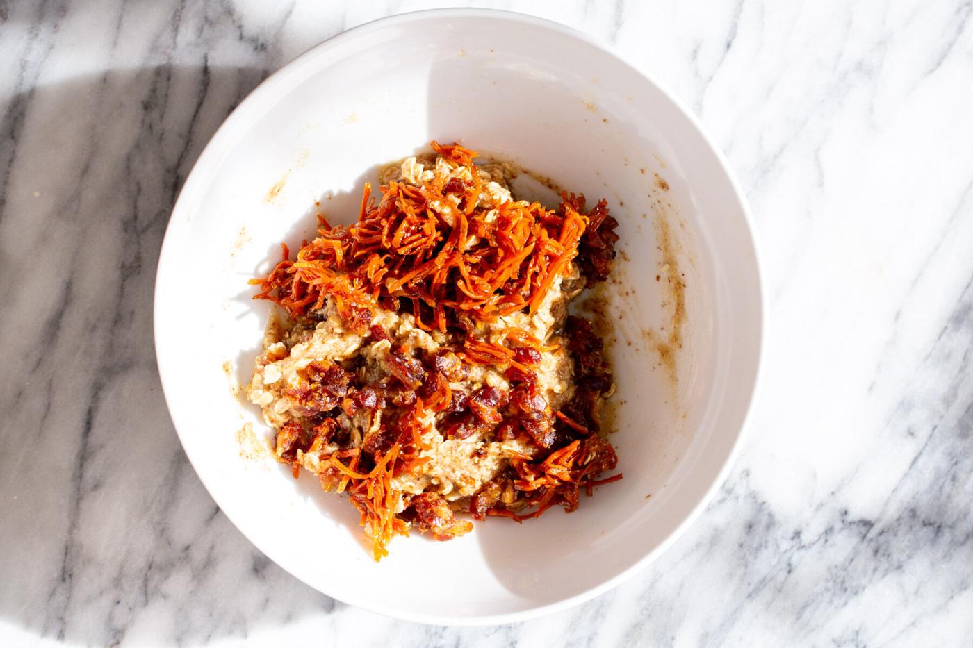 caramelized carrots being added to oatmeal cookie dough in a white bowl