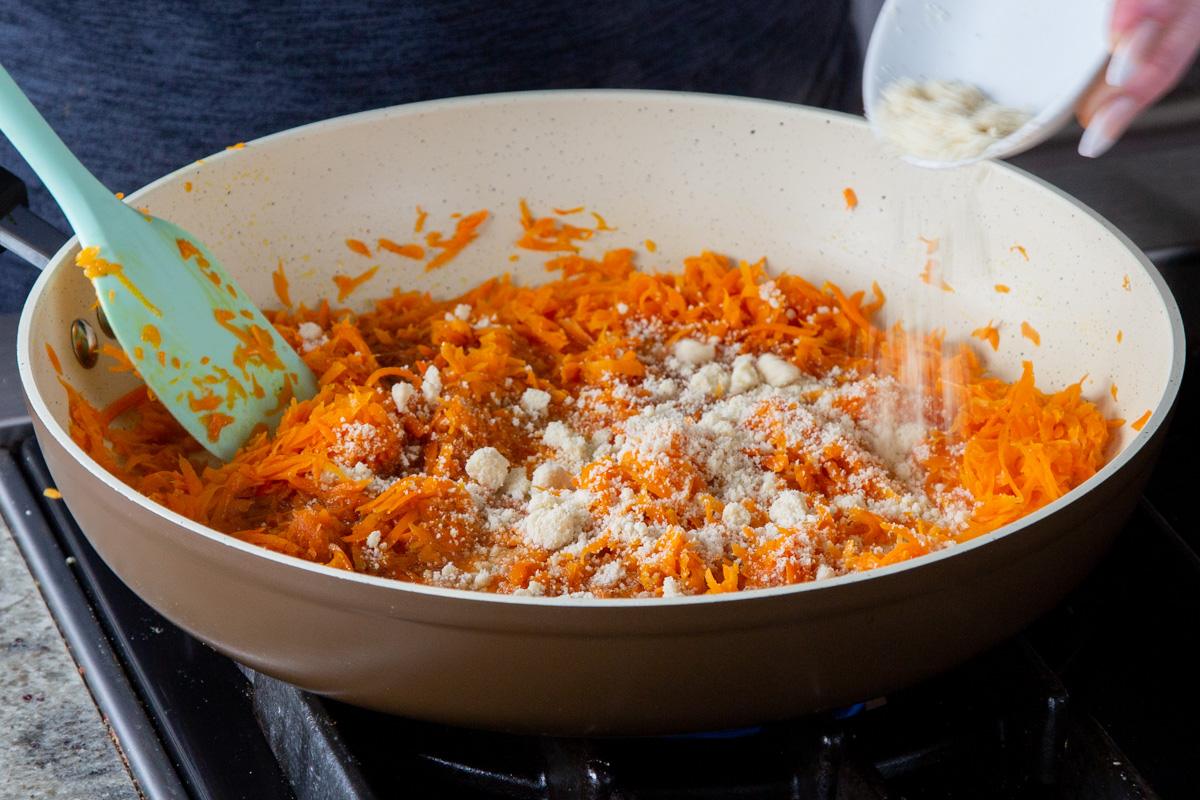 adding almond flour to the shredded carrot mixture in the pan