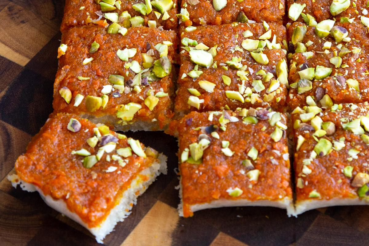layered carrot halwa coconut burfu bars topped with chopped pistachios