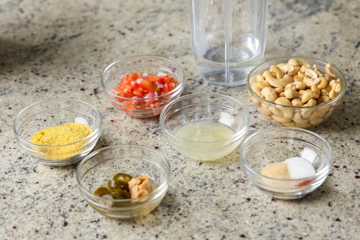 cashews, tomato, and other nacho cheese ingredients in bowls on the kitchen counter