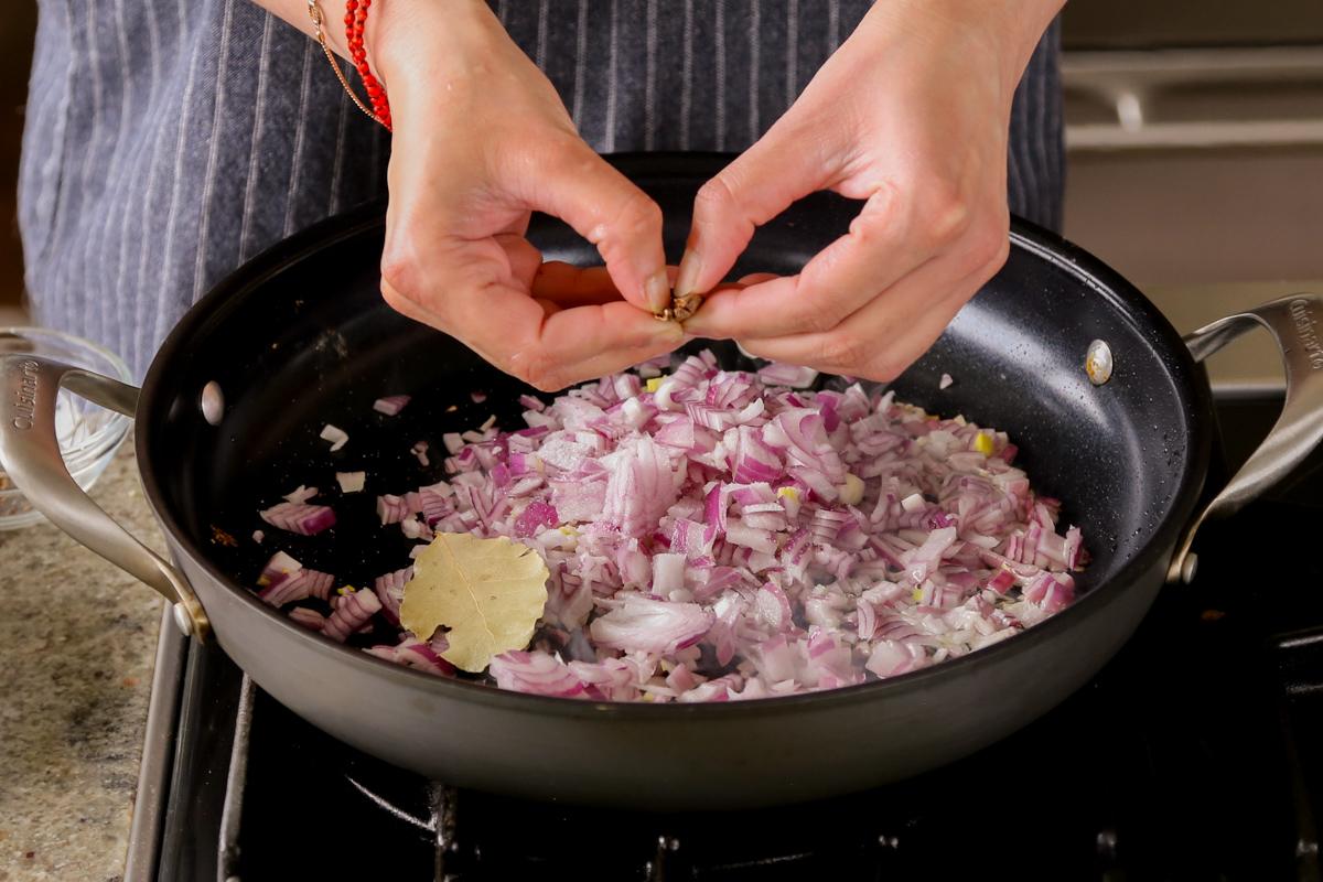 adding cardamom pod to the pan of onion and whole spices