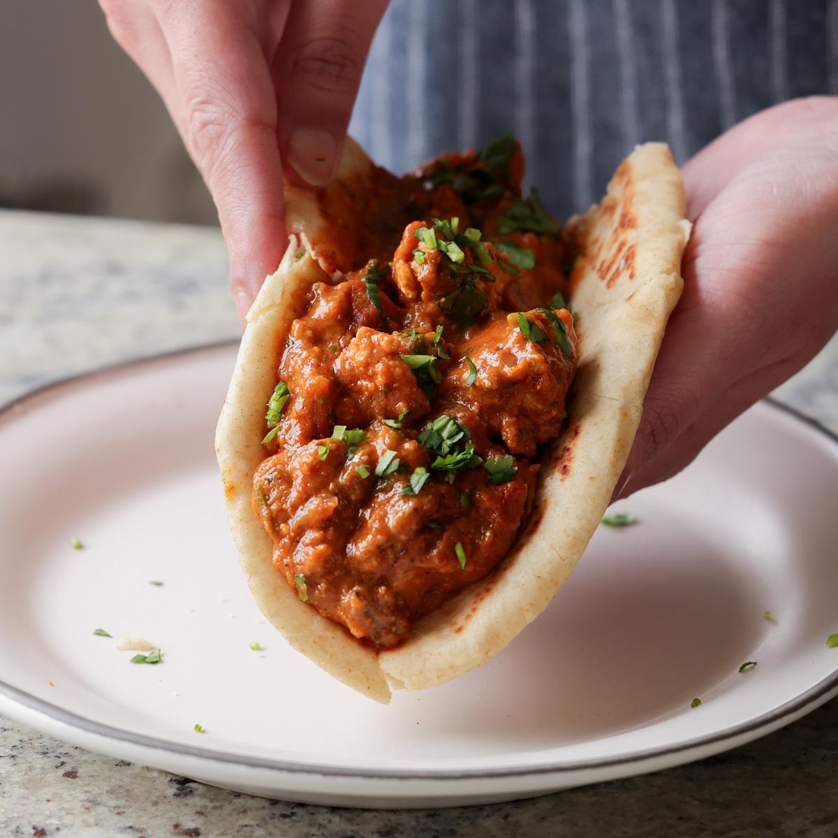 hands holding chicken angara folded into a piece of flatbread