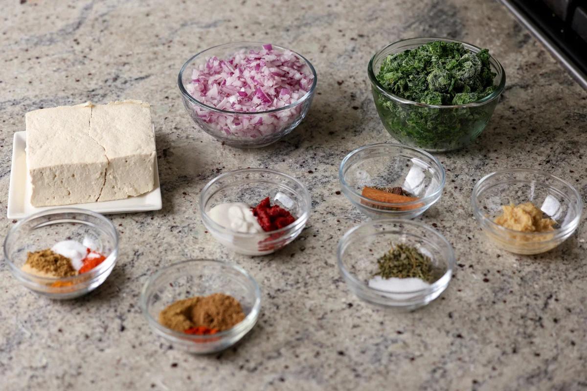 spinach, onions, spices, and other vegan chicken saagwala ingredients in bowls on the kitchen counter