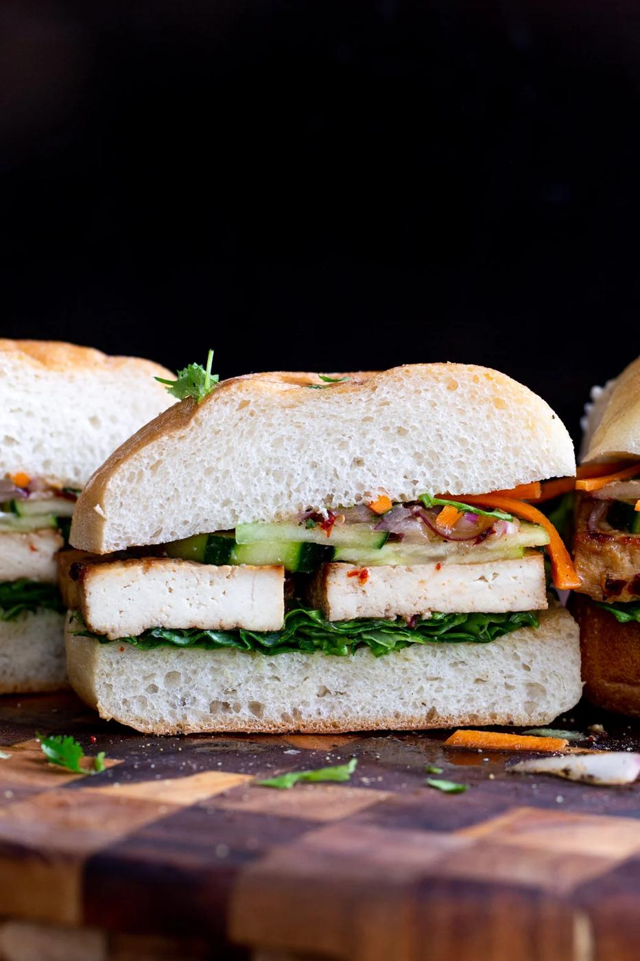 a vegan lunch sandwich sliced in the middle filled with baked tofu and topped with veggies