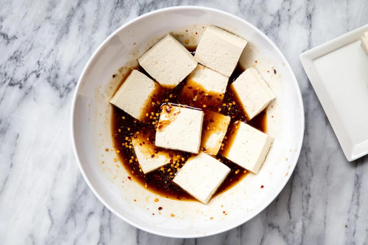 sliced tofu being added to a bowl with marinade
