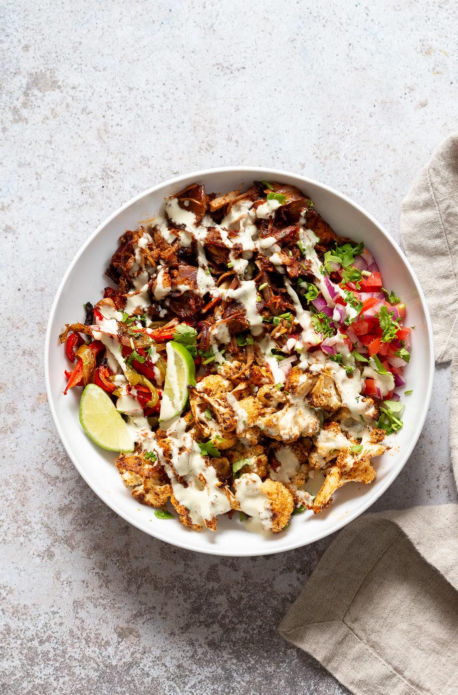Chili Lime Roasted Veggies & Jackfruit drizzled with jalapeno cream sauce in a White Bowl