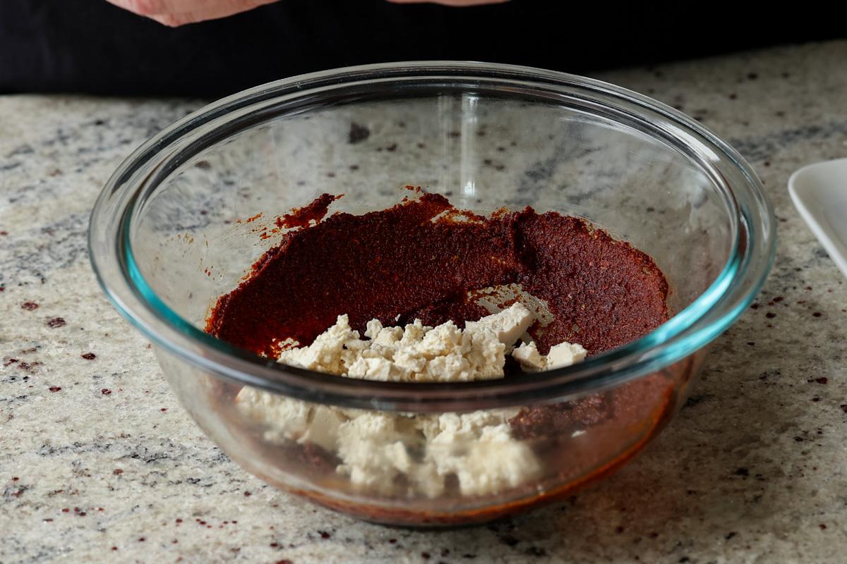 adding crumbled tofu to the bowl of seasonings
