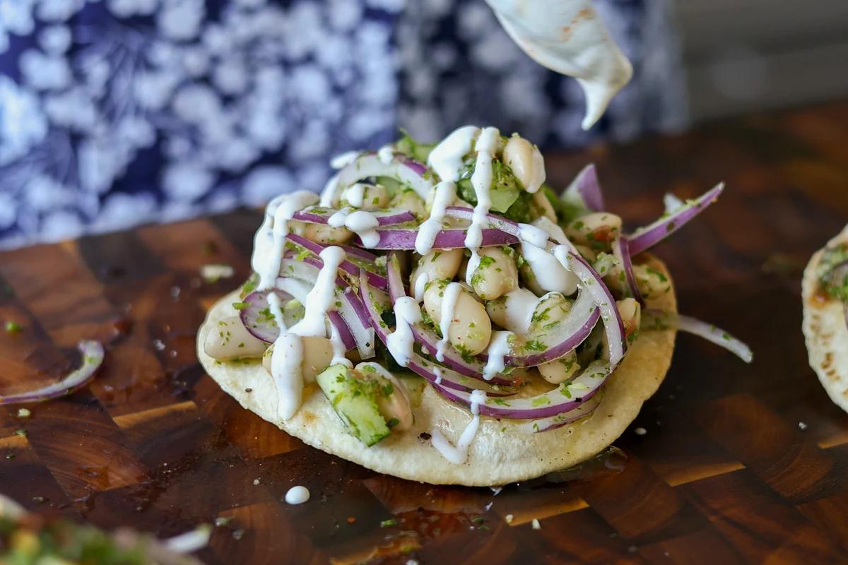 adding the yogurt drizzle to the chutney bean tostadas