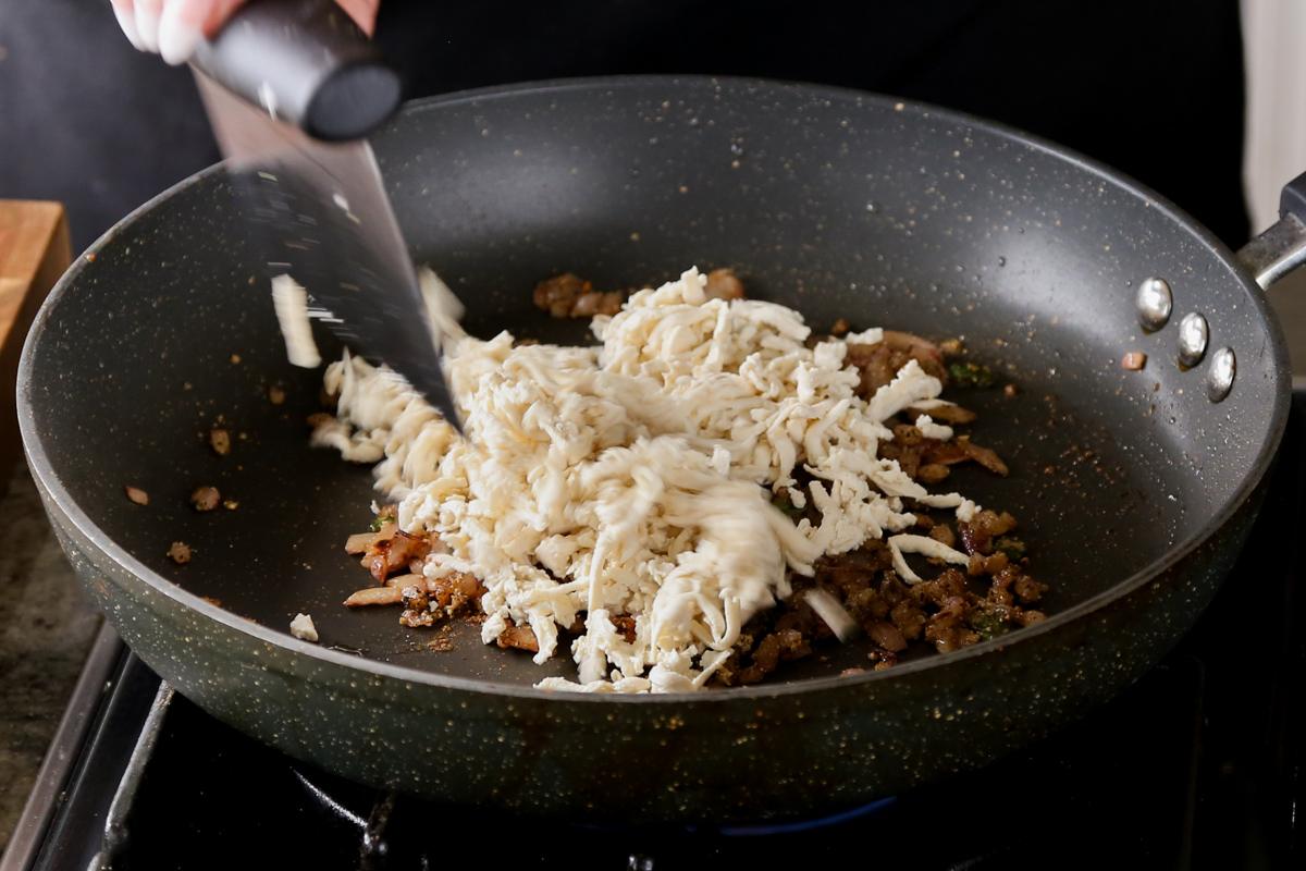 adding shredded tofu to the pan with onion