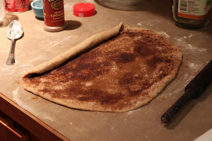 rolled out and filled cinnamon roll dough being rolled up to shape buns