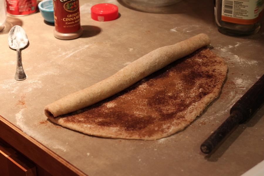 cinnamon filled dough rectangle being rolled into a roll to make vegan cinnabons