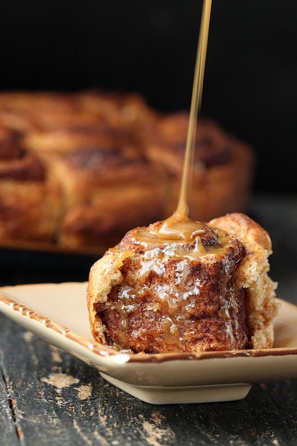 side view of a homemade fluffy and soft vegan cinnamon roll being drizzled with maple icing