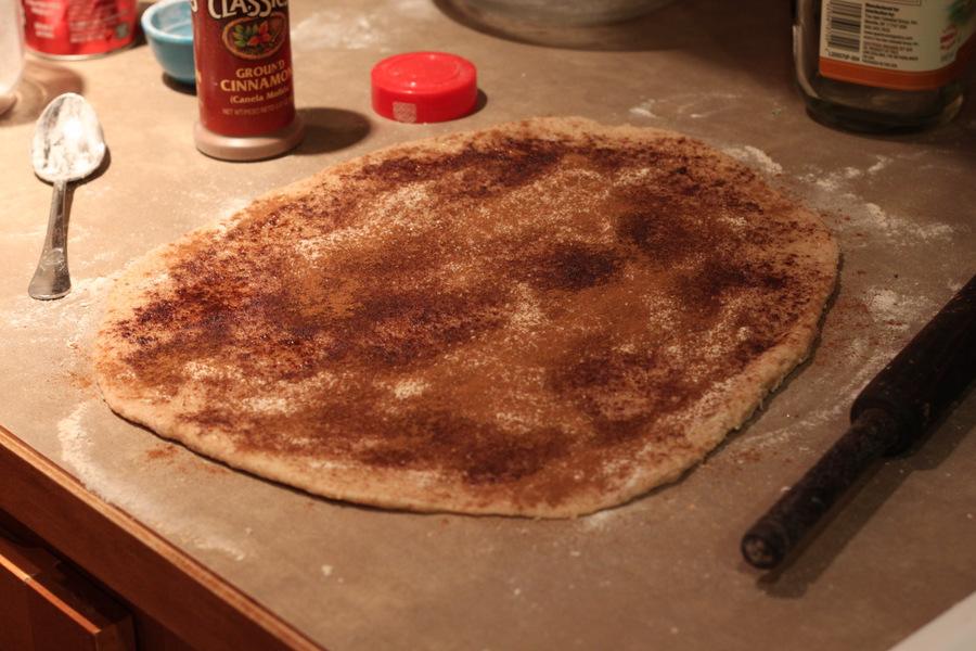 cinnamon being sprinkled liberally on top of cinnamon roll dough