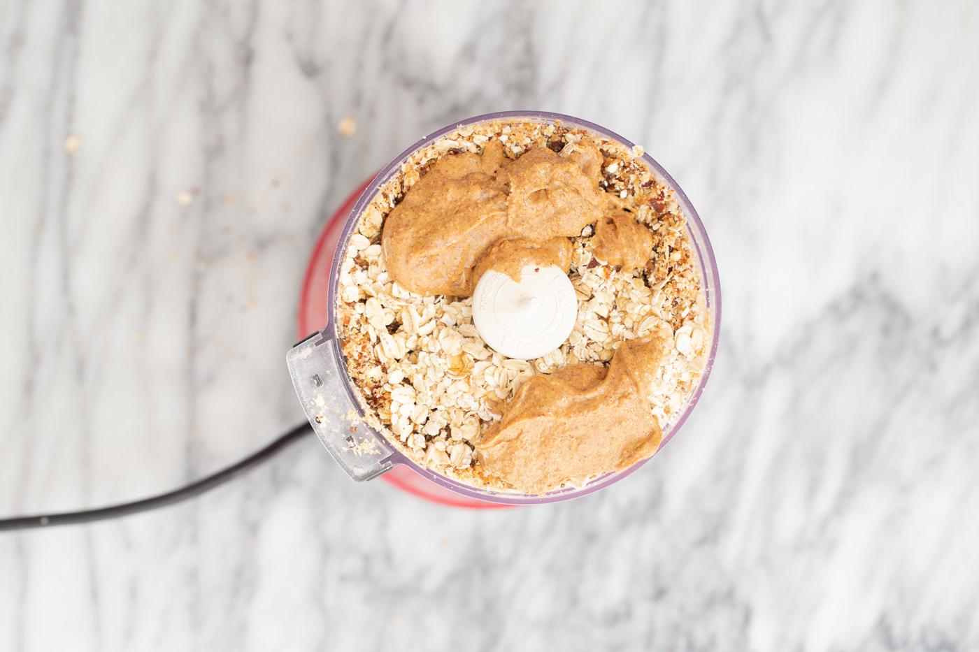 almond butter being added to blended dates, nuts and oats to make vegan date bars