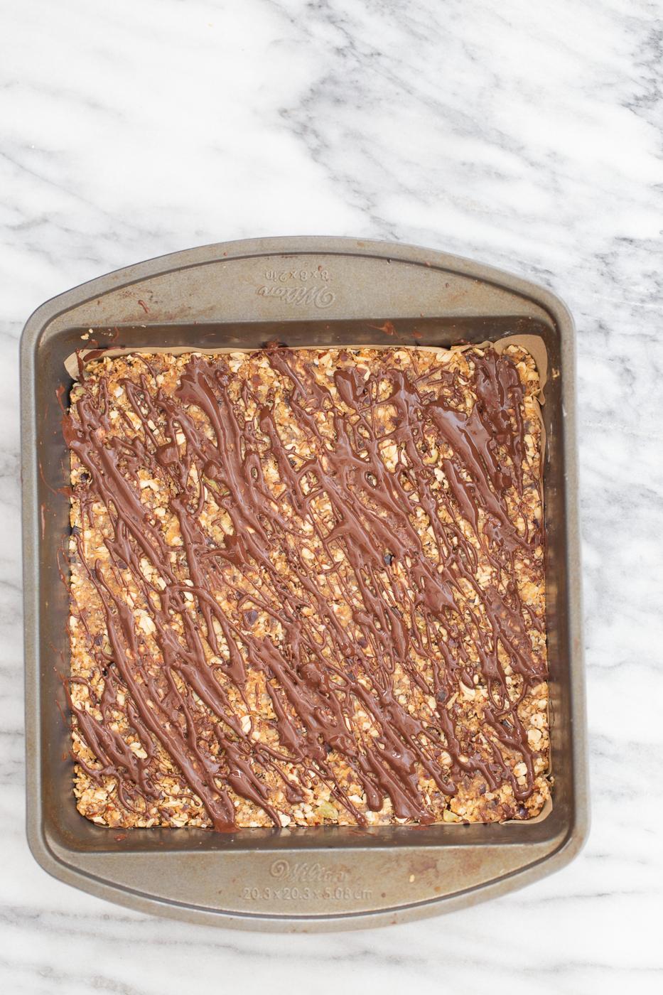 overhead shot of a casserole dish with vegan coconut caramel date bars drizzled with melted chocolate