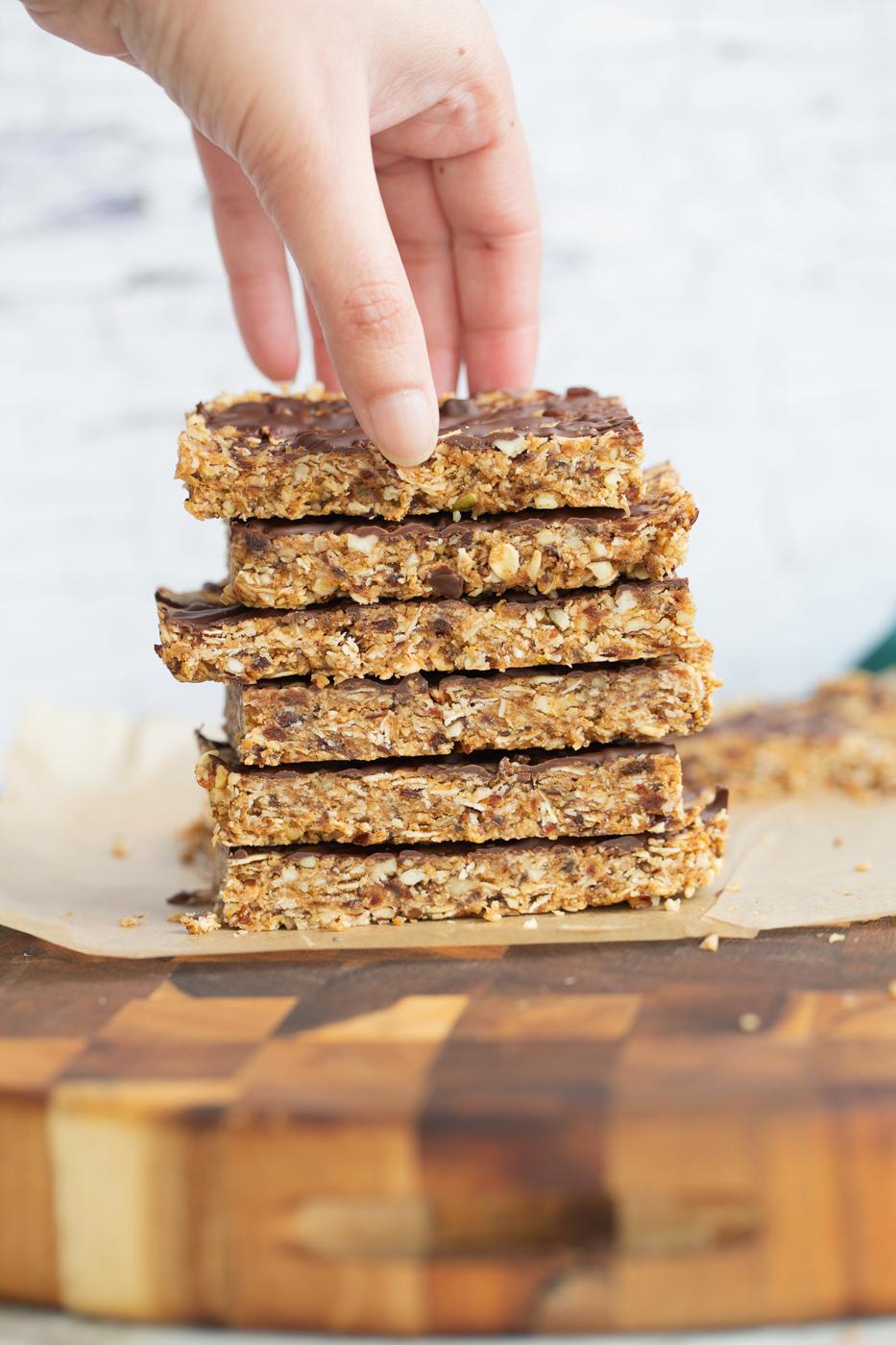 a hand reaching for a vegan date bar on top of a stack of vegan snack bars