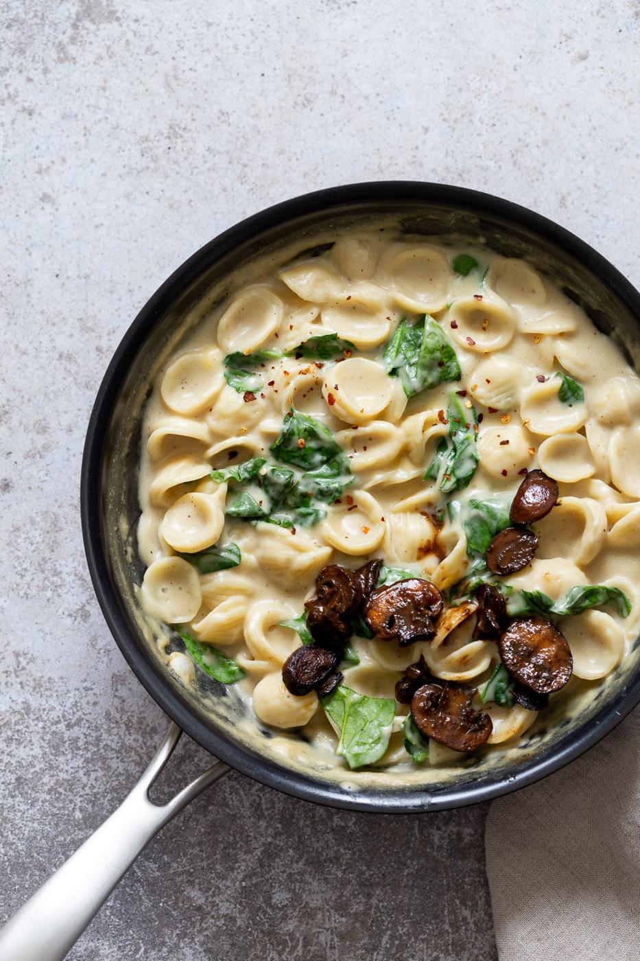 overhead shot of a black pot with creamy vegan spinach pasta topped with balsamic mushrooms