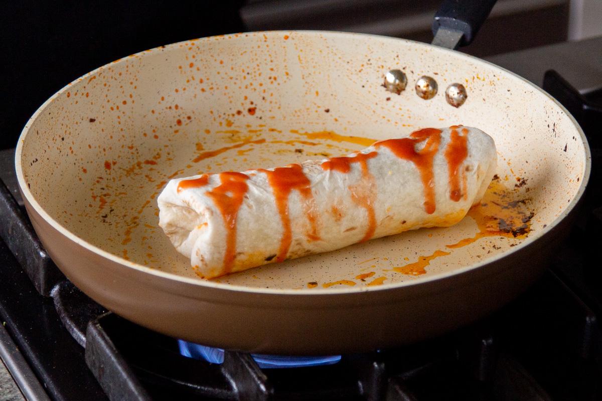 sealing the crispy tofu burrito with hot sauce in a pan