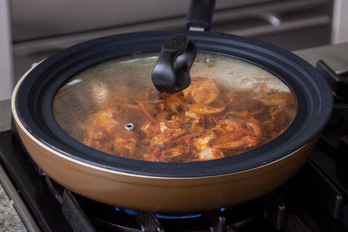 tofu and mushrooms cooking in the pan with the lid on