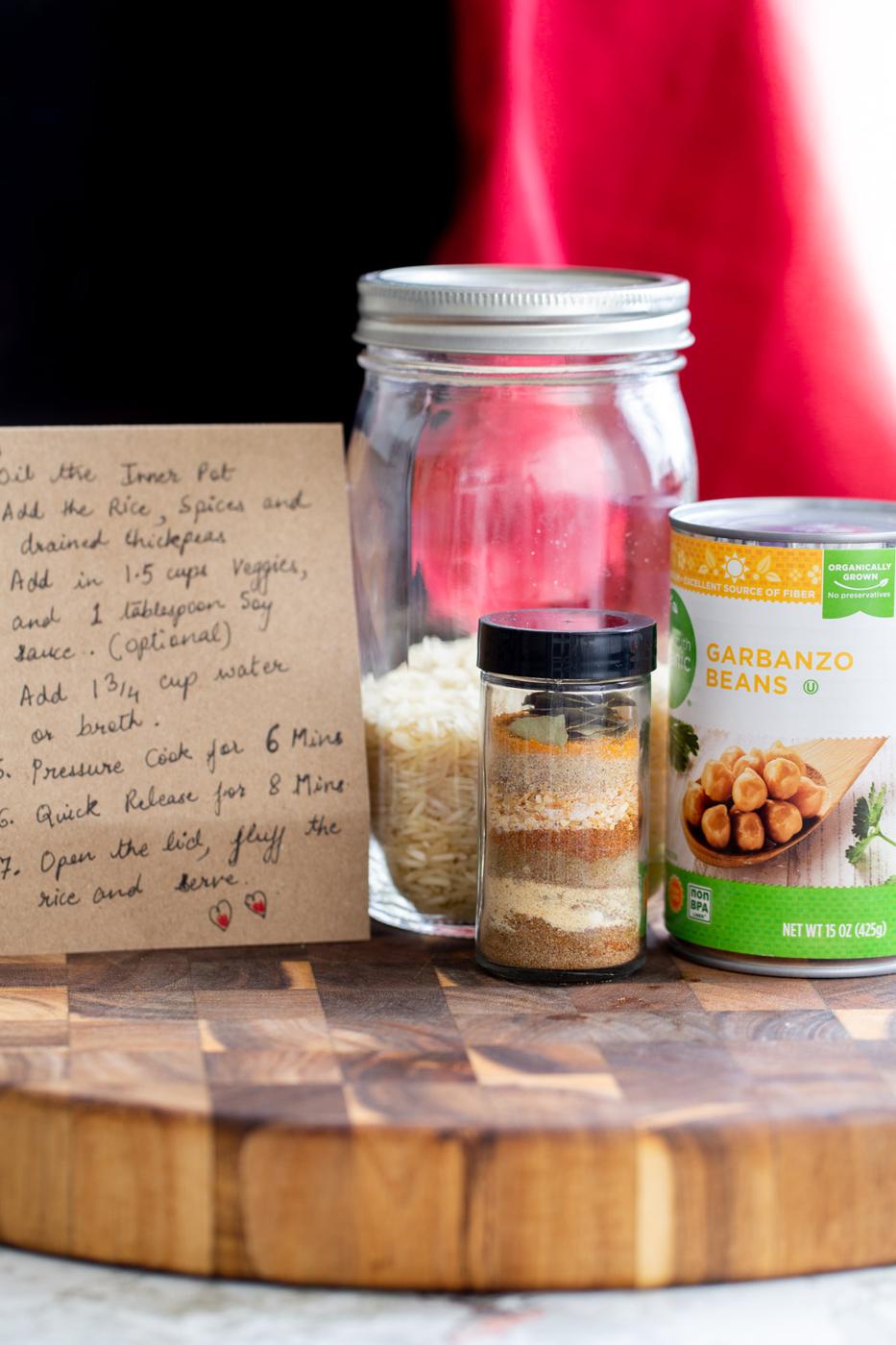 a recipe card, spice mix, can of chickpeas and a mason jar with rice on a wooden board