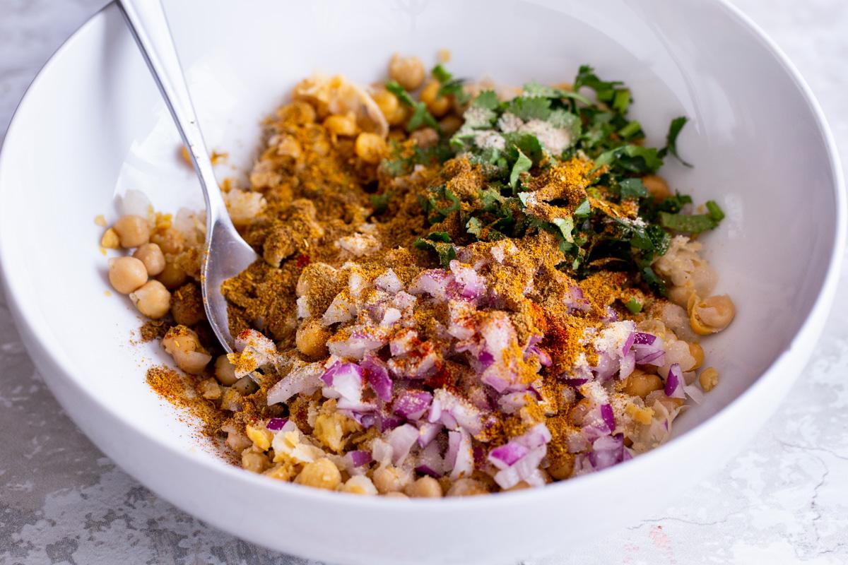 spices, onions and herbs being mixed with mashed chickpeas to make vegan egg salad