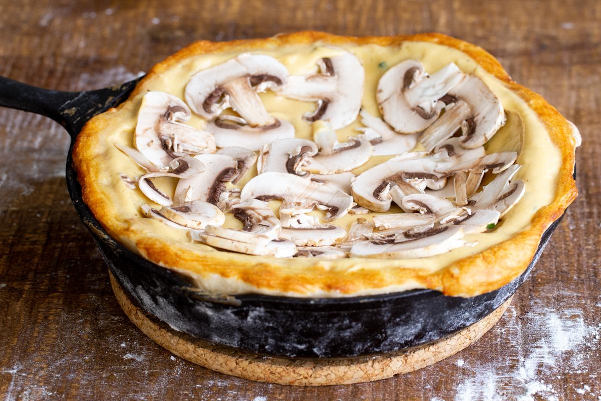 a prebaked vegan deep dish pizza topped with cheese sauce and sliced mushrooms