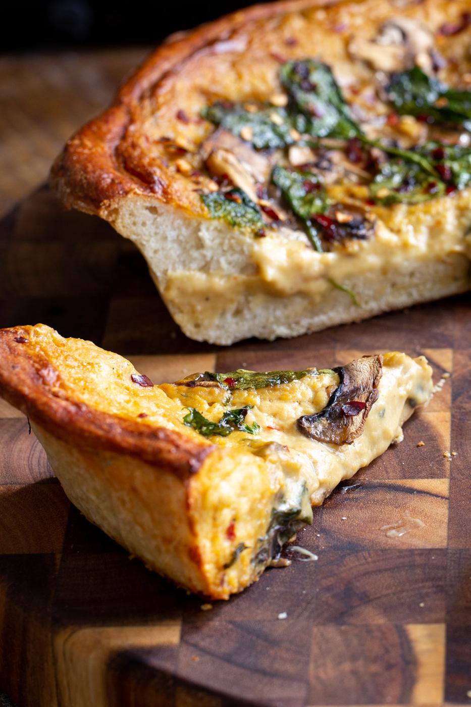 sliced vegan deep dish pretzel crust pizza on a wooden board
