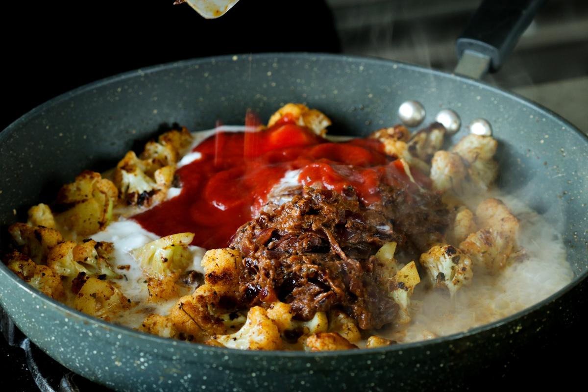 adding tomato puree and do pyaza sauce to cauliflower in the pan