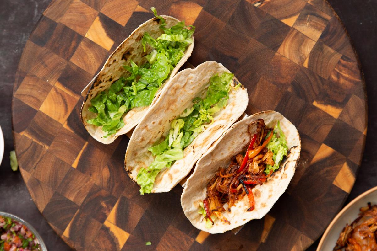 three tacos being assembled with lettuce and jackfruit
