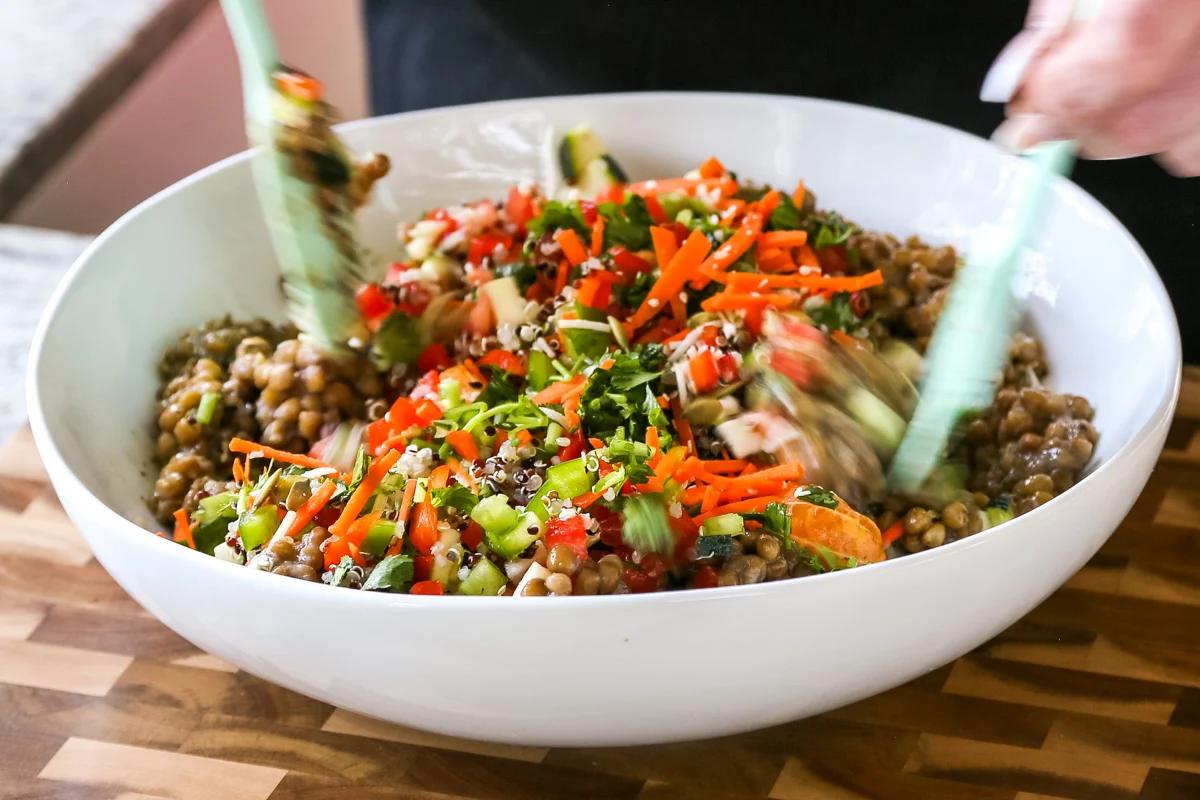 mixing lentil quinoa salad with veggies in a bowl