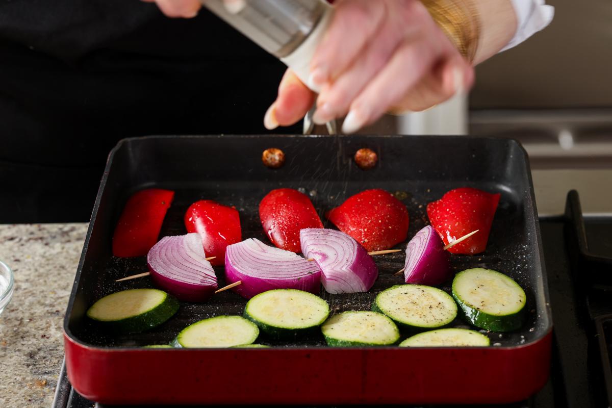 cracking fresh pepper onto the vegetables on the grill pan