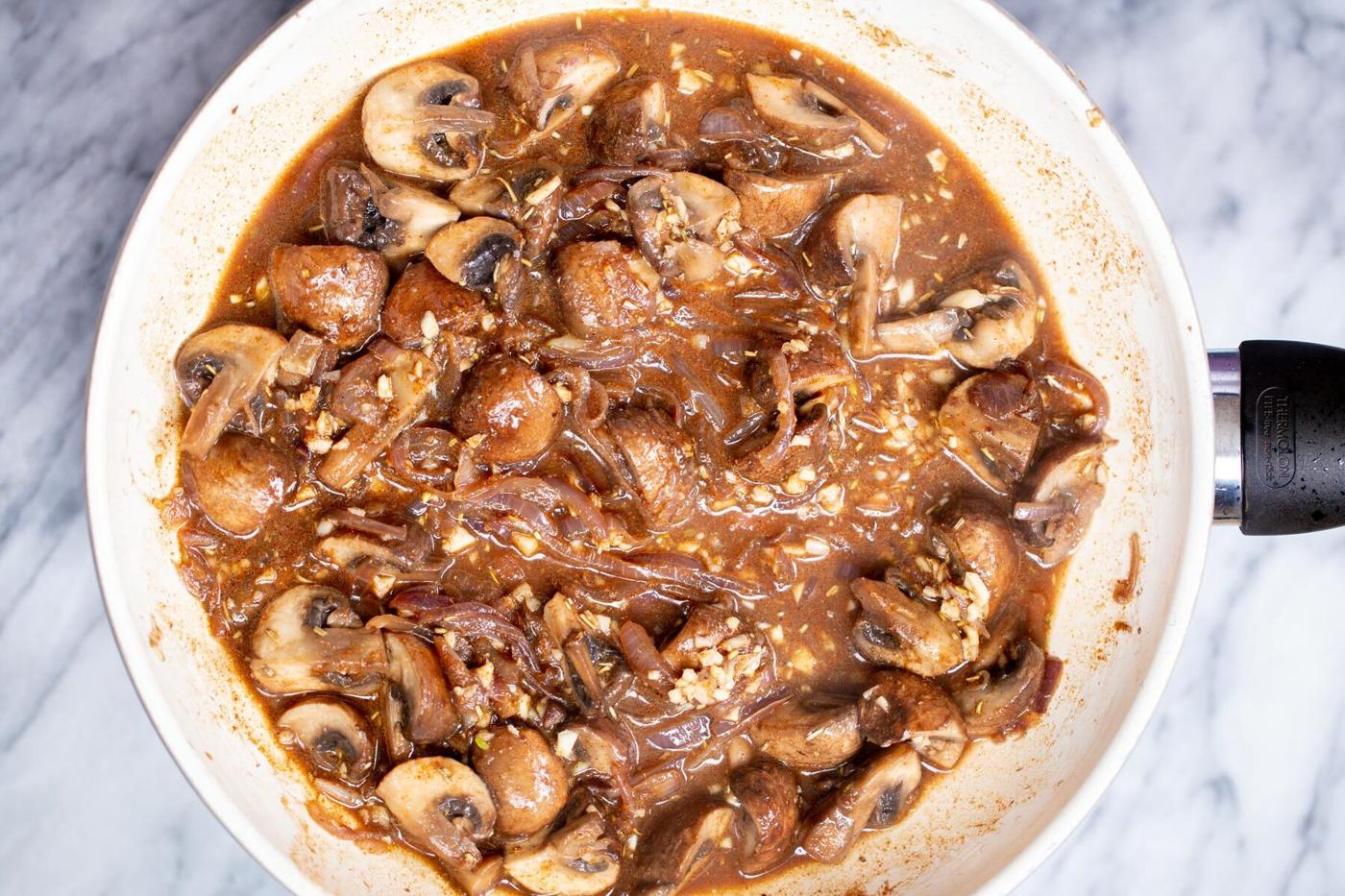 mushrooms simmering in a white sauteeing pan