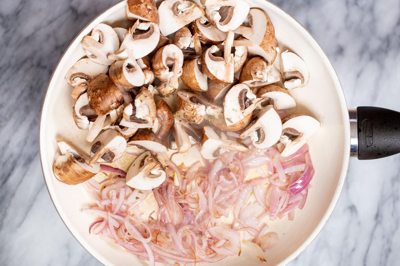 mushrooms and onions in a white sauteeing pan