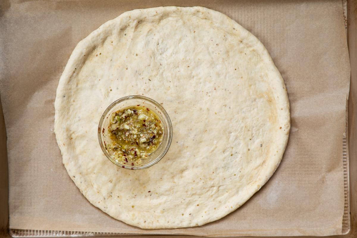 shaped pizza dough on a baking sheet with a small dish of seasoned oil