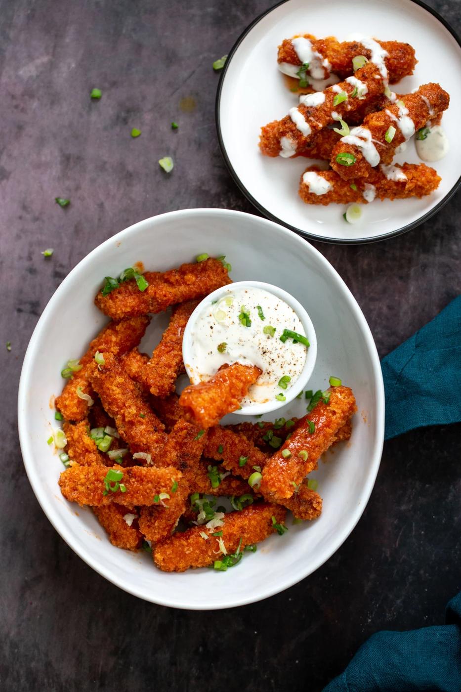 a bowl with firecracker tofu wings served with a dip and a small plate with vegan tofu wings drizzled with ranch