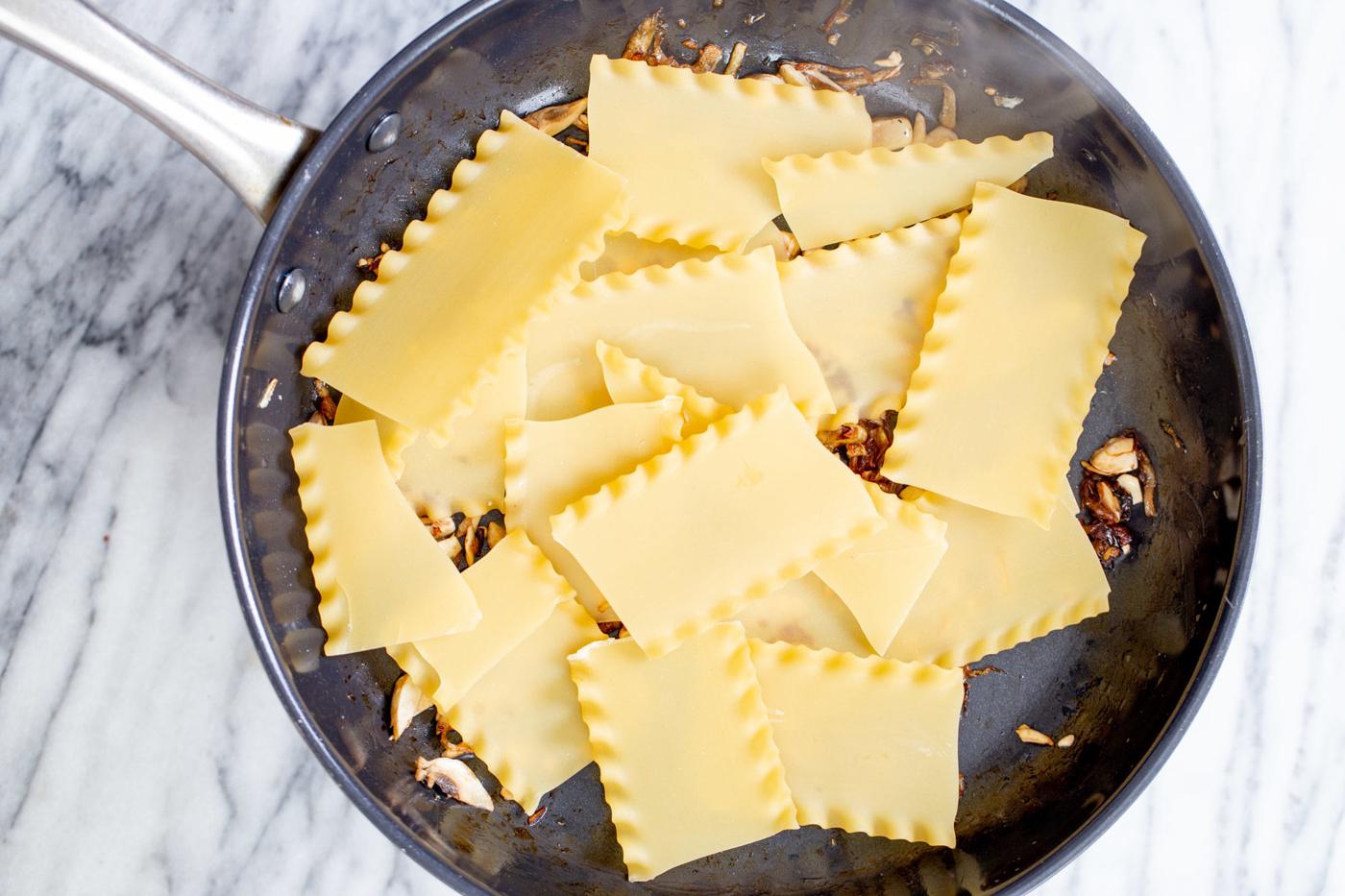 lasagna noodles being added to a skillet to make skillet lasagna