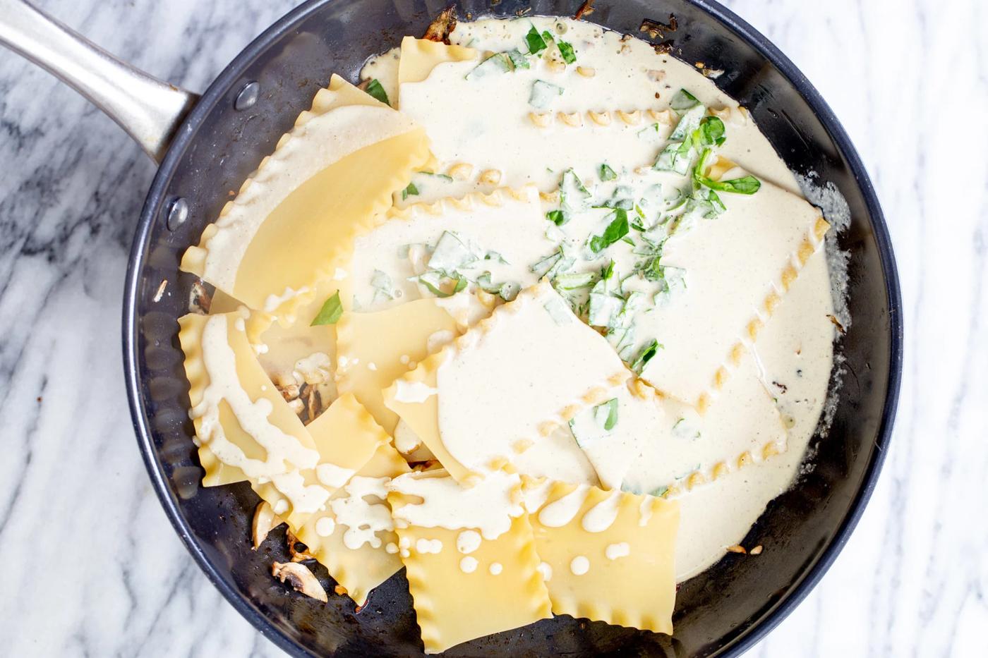 vegan bechamel sauce being added to lasagna noodles and caramelized onion is a pan