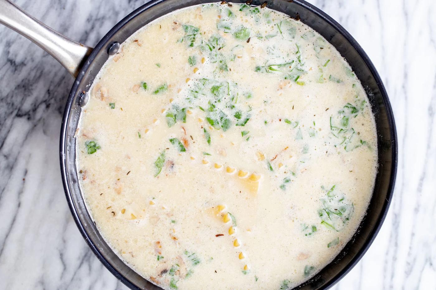 overhead shot of a skillet with lasagna pasta cooking in vegan bechamel