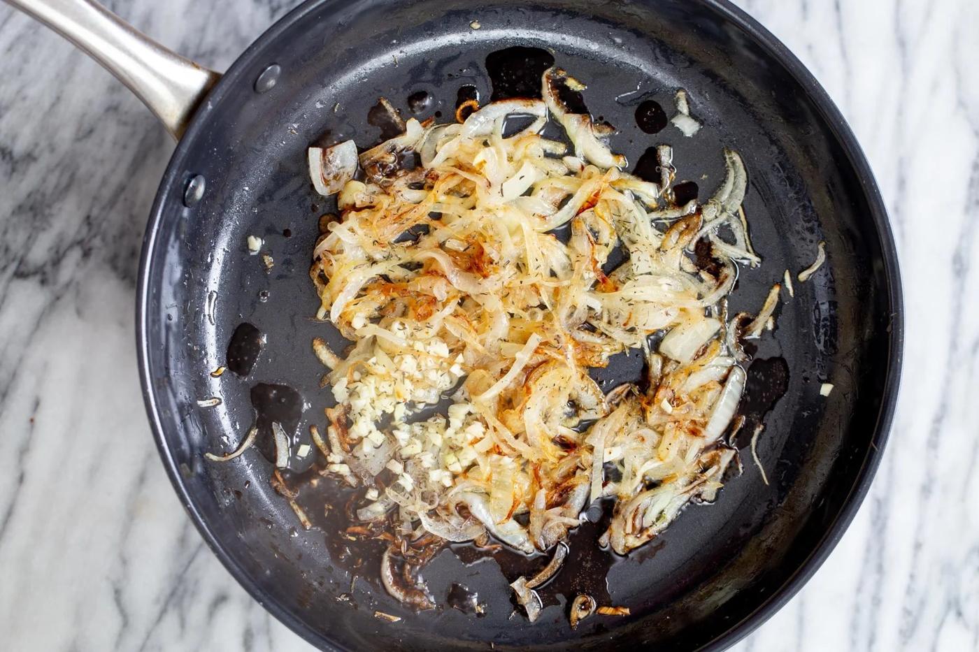 garlic being added to caramelized onion slices in a skillet