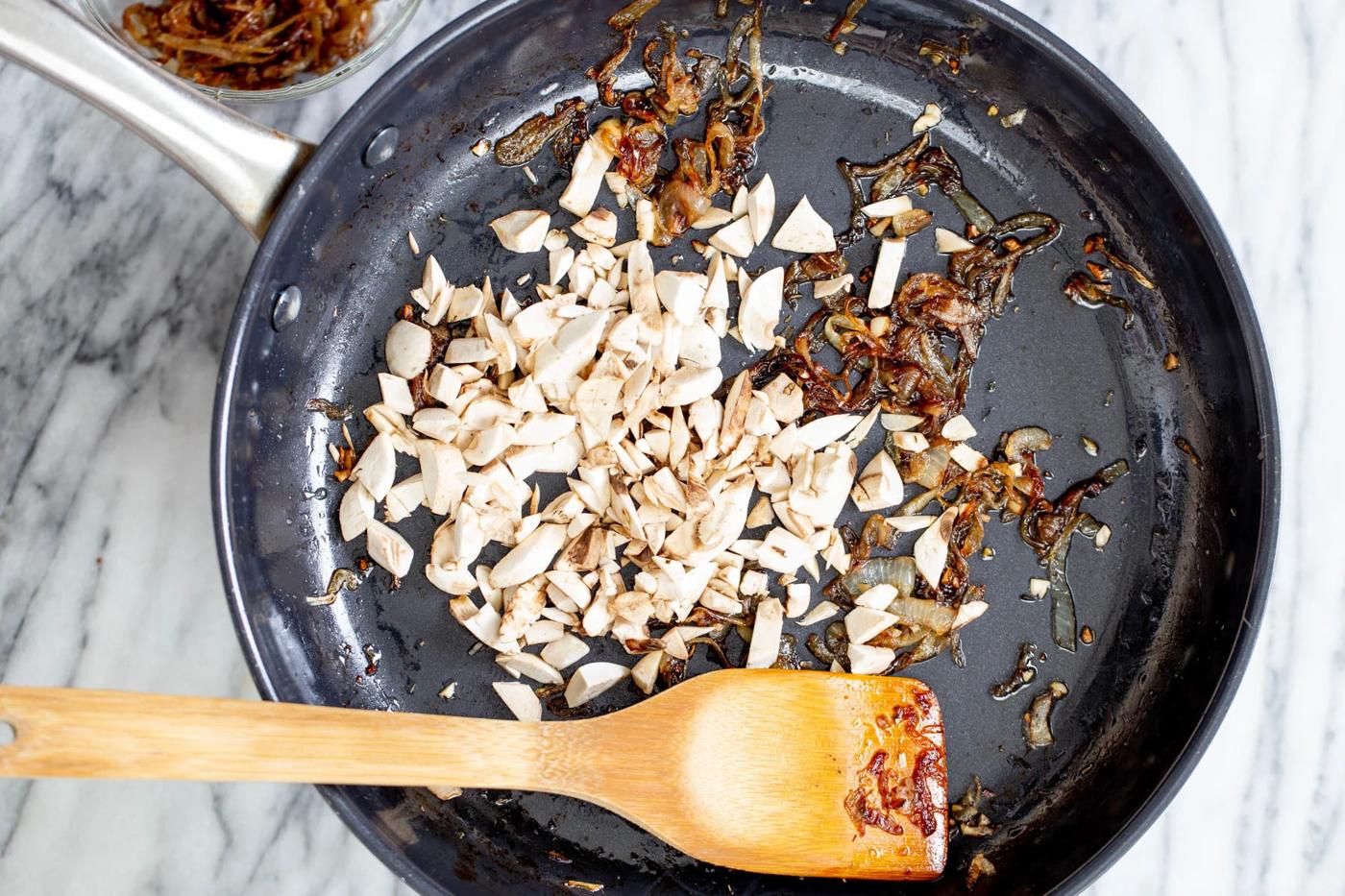 mushrooms being added to caramelized onions in a skillet