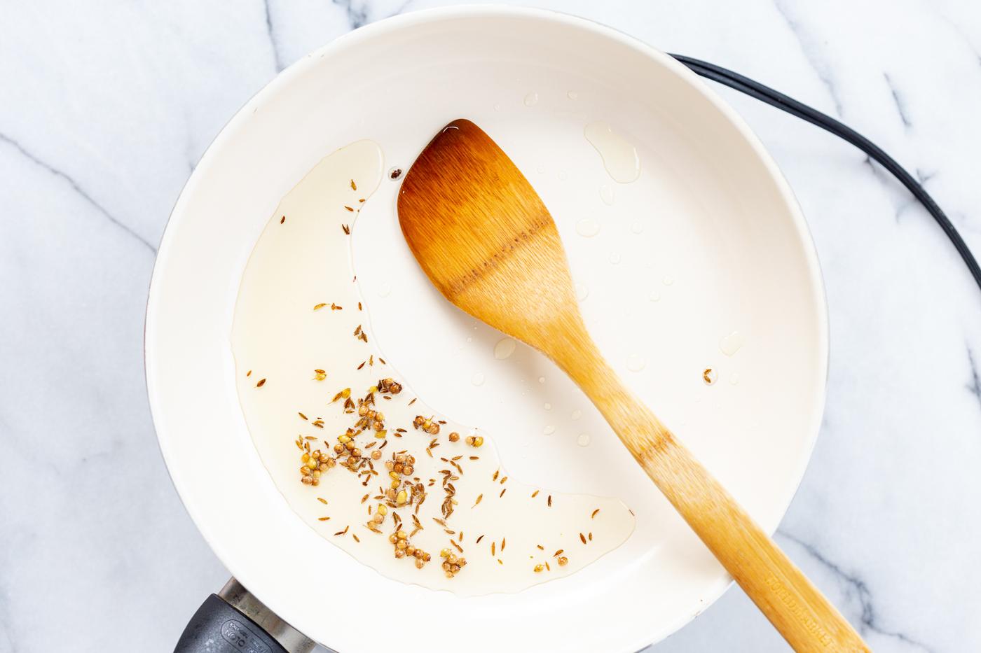 Spices in oil in a white skillet