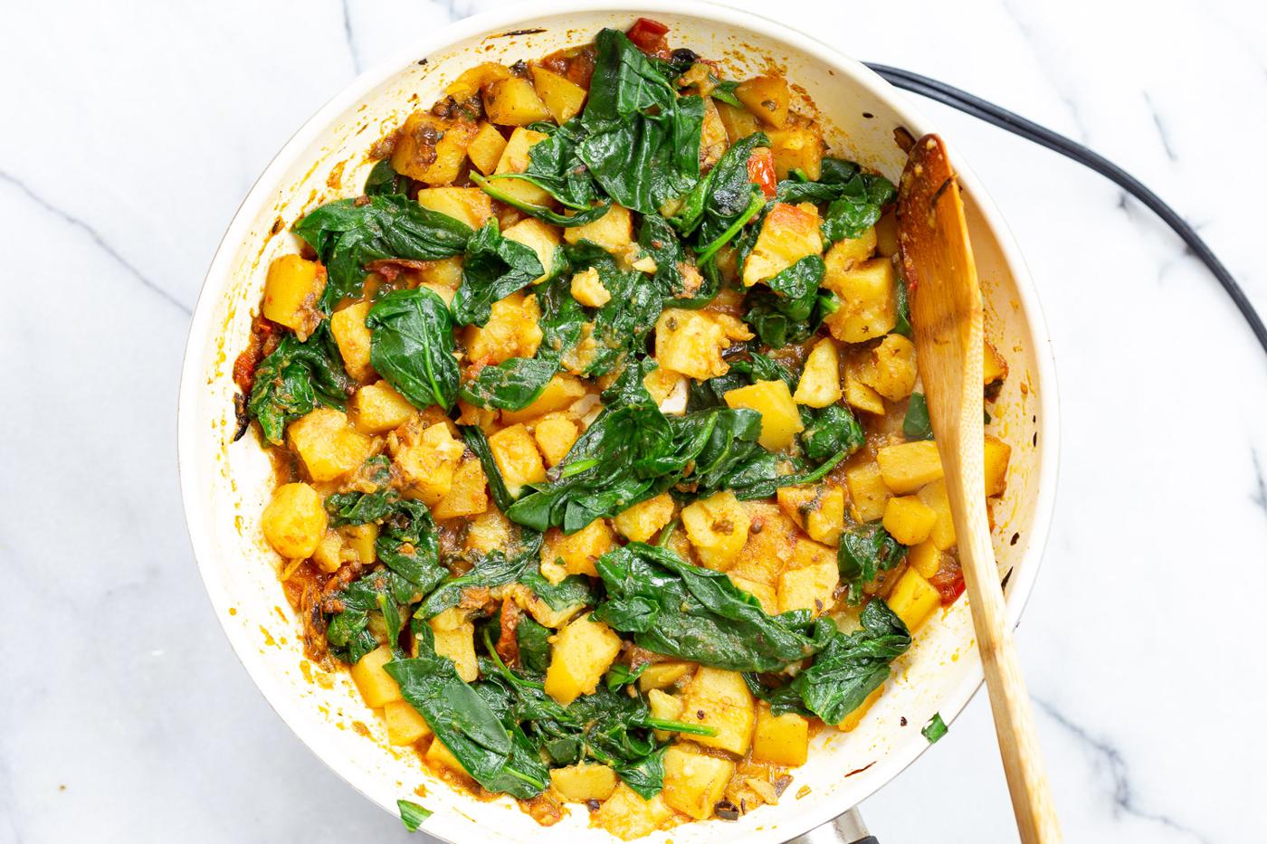 Spinach Potato and tomato curry in white skillet