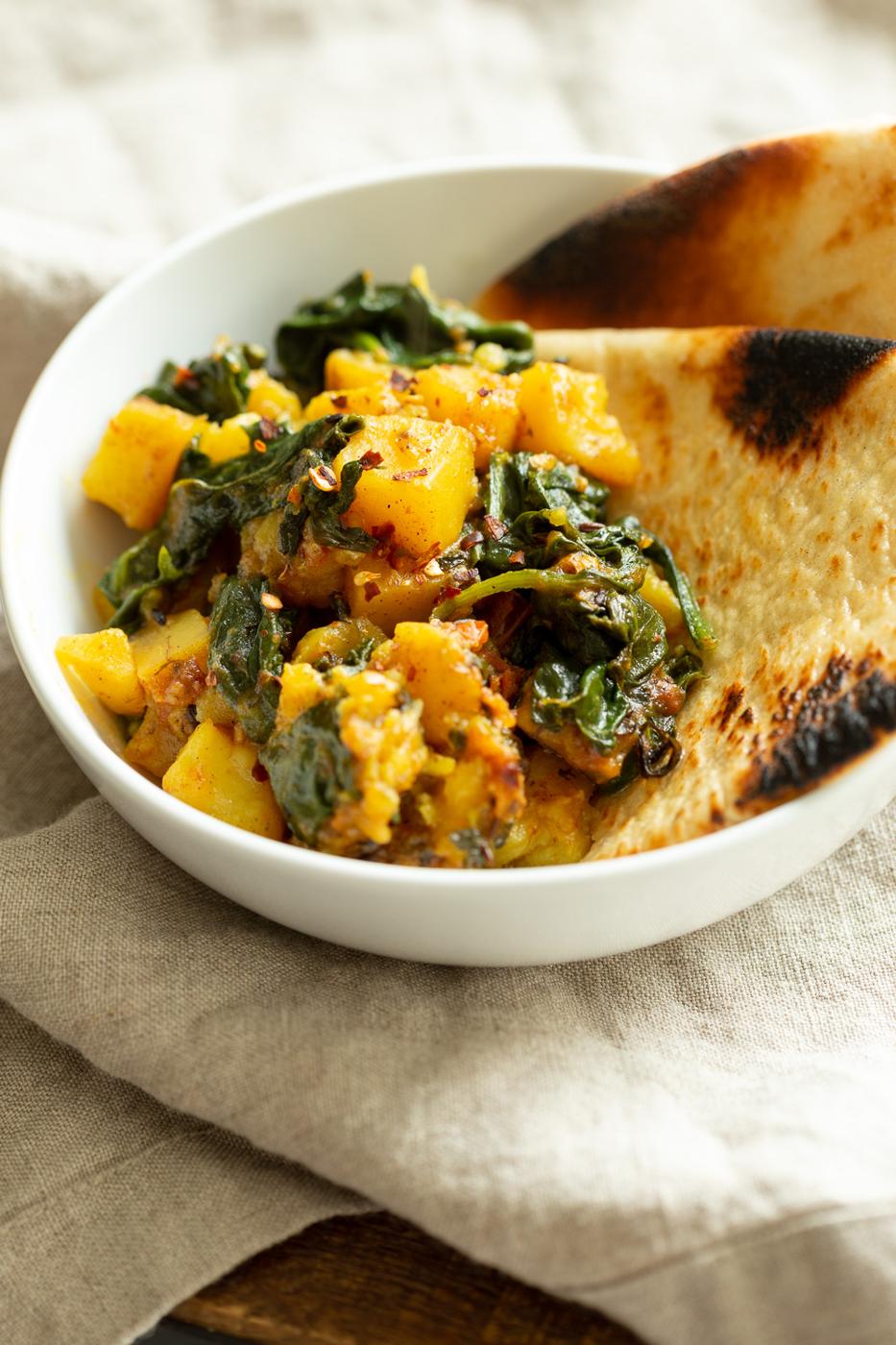 Garlic Potato Spinach Stir fry with Naan bread in a white bowl