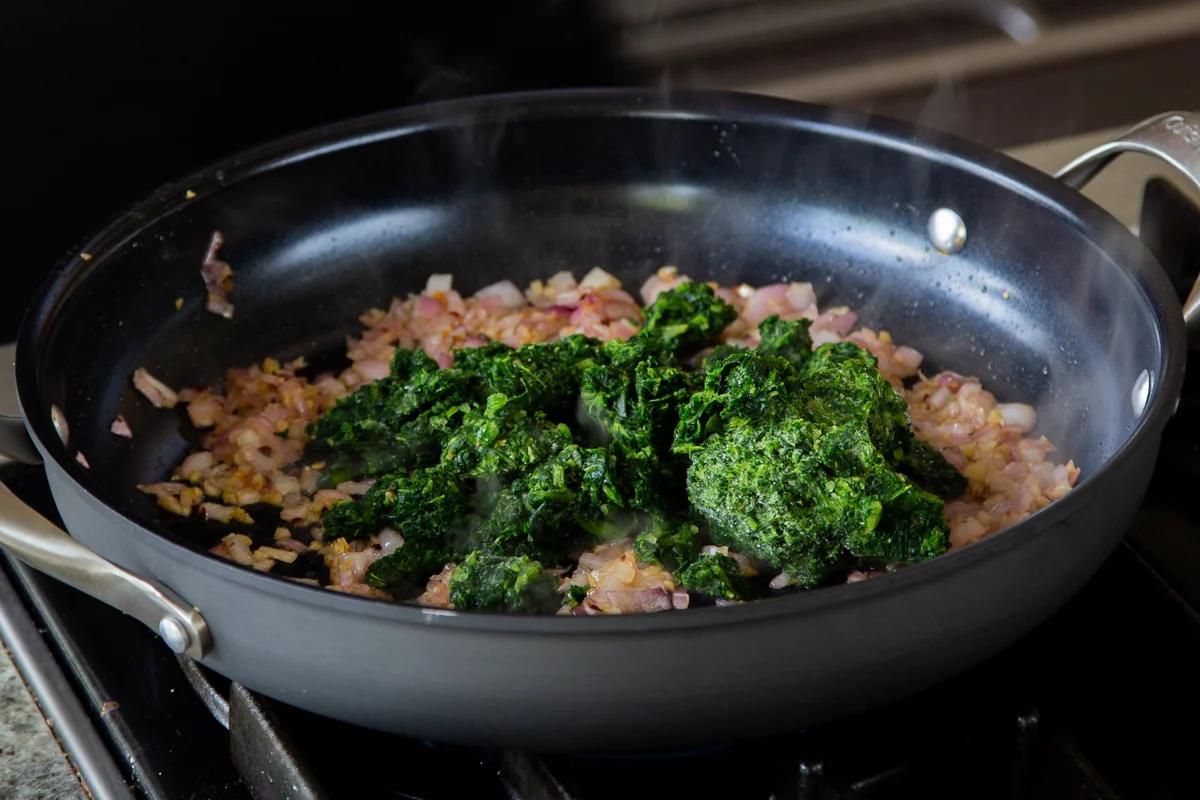 adding spinach to the cooked onions and garlic in the pan
