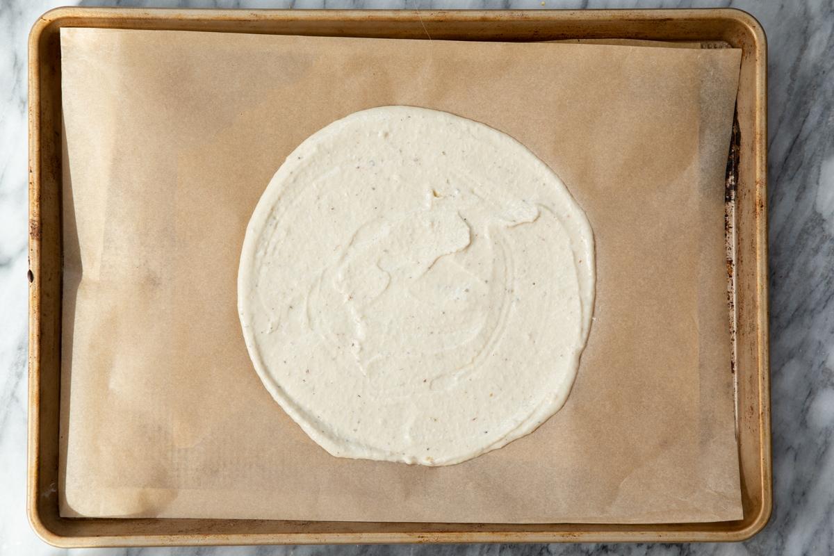 almond flour pizza dough being spread on a baking sheet