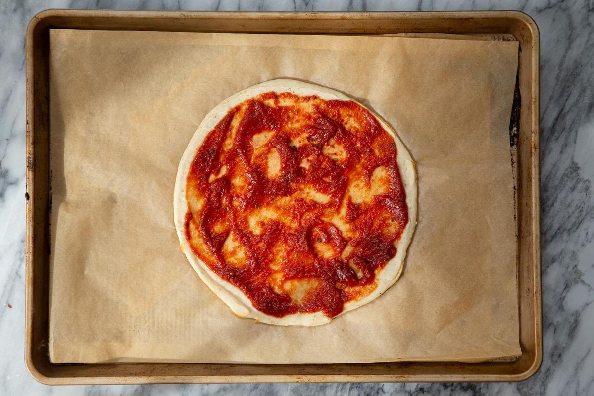 marinara being spread on prebaked almond flour pizza crust