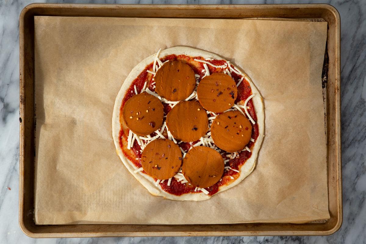 almond flour pizza crust being topped with pepperoni and vegan cheese
