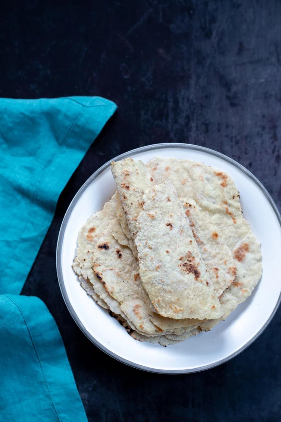 Gluten free Cauliflower flatbread rolled up and stacked on a white plate with turquoise napkin