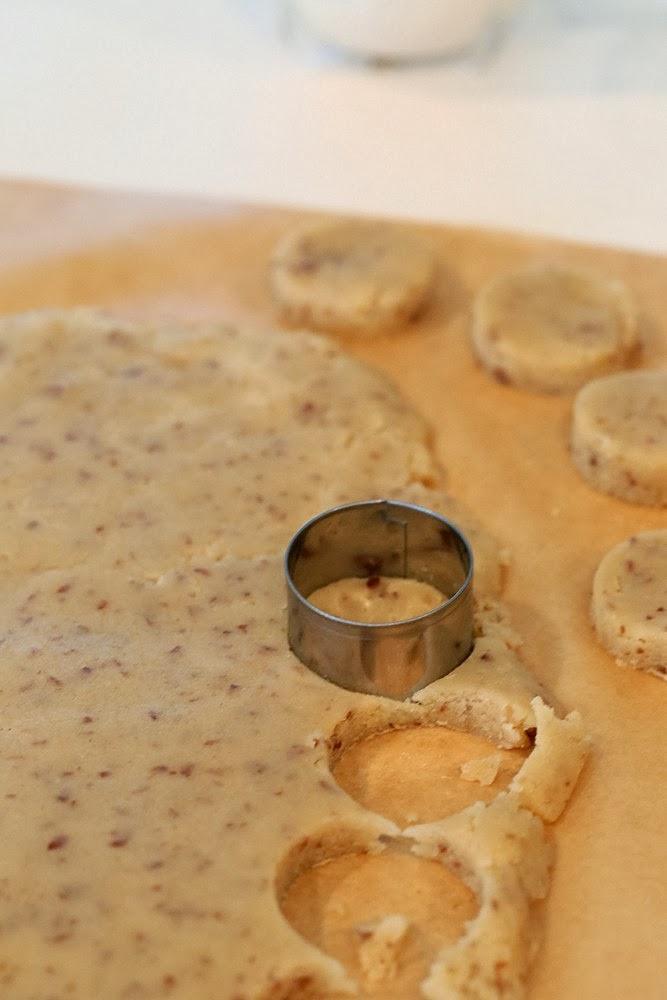 rolled out vegan cookie dough being cut into sugar cookies with a round metal cookie cutter